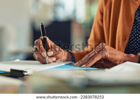 Close up of african american business woman hands writing on report while working in office. Successful black woman signing documents at home. Mid adult freelancer signing contract document on table.