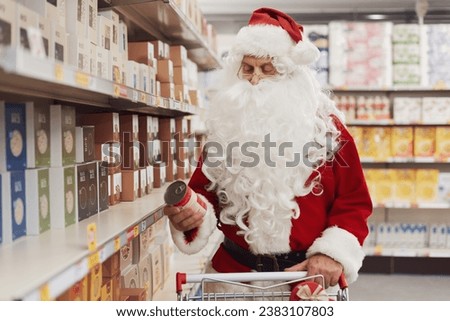 Funny Santa Claus doing grocery shopping at the supermarket, he is buying cheap canned food Royalty-Free Stock Photo #2383107803