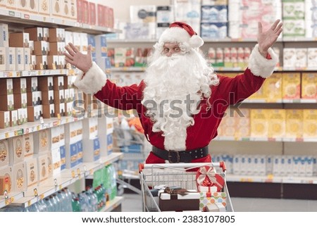 Happy Santa Claus doing grocery shopping at the supermarket, he is smiling with raised arms and looking at camera Royalty-Free Stock Photo #2383107805