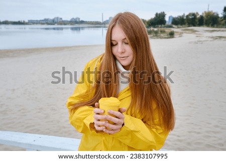 Happy girl in a yellow raincoat walks along the beach of a lake or river on a cool day. Travel concept. Girl on a journey. Amazing scenic street view