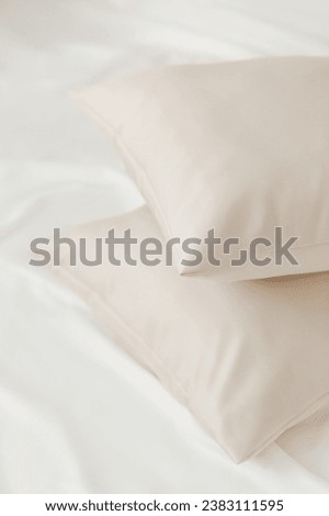 Two beige pillows in satin or silk or lyocell pillowcases on white sheet. Bedding and accessories. Home textile Royalty-Free Stock Photo #2383111595