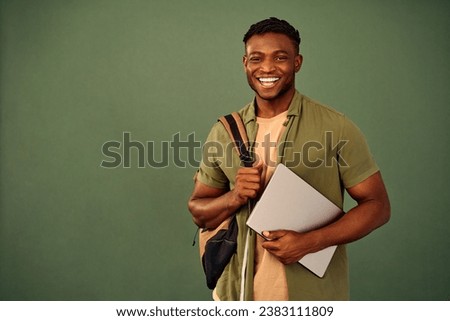 Distance learning. Glad african american guy with backpack and wireless laptop posing over green background. Enthusiastic smiling student engaging in online education with help of modern gadget.