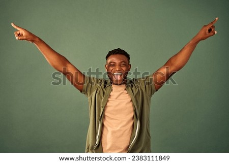 Cheering in success. Joyful handsome african guy wearing casual yellow t-shirt and unbuttoned shirt posing over green background with hands wide open. Sincere human reaction on amazing news.