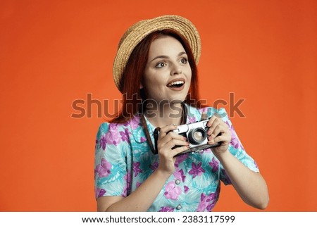 Close up of amazed woman holding old film camera, looking at the attractions around and smiling, isolated on orange background. Portrait of female traveler.