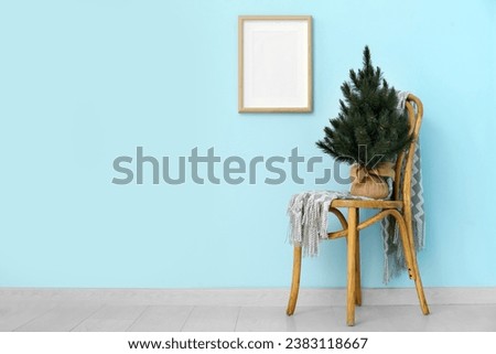 Christmas tree on chair near blue wall with blank frame in room
