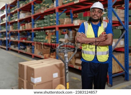 Portrait of male supervisor standing at storage shelf in warehouse with his arm crossed looking at camera. Confident multiracial logistic manager employee in safety uniform working with stock in store