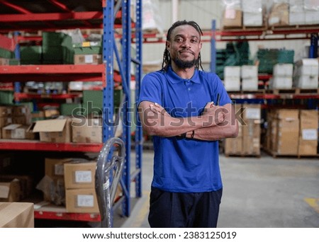 Portrait of male supervisor standing at storage shelf in warehouse with his arm crossed looking at camera. Confident multiracial logistic manager employee in safety uniform working with stock in store