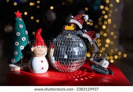 models of toy excavators, a mirrored disco ball, a snowman, bokeh from holiday garlands. shooting in the dark, highlighting with light. Business concept for Happy New Year greetings