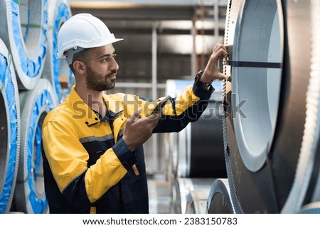 Male factory worker inspecting quality rolls of galvanized or metal sheet in in aluminum material warehouse. Male worker working in warehouse of raw materials during manufacturing process in plant Royalty-Free Stock Photo #2383150783