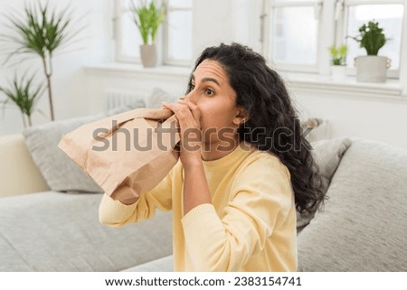 Young woman alone at home with a panic attack shortness of breath, trembling, numbness, loss of consciousness. Side view of a female suffering an anxiety sitting on a couch. Chest pain, fear symptom