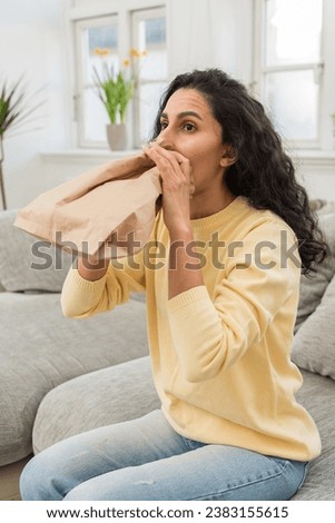 Vertical photo of a girl holding a paper bag near her mouth, having a panic attack, the girl is breathing heavily, trying to restore her breathing and control her heartbeat. Emergency help at home