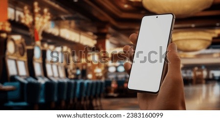 CU 30s Caucasian male holding a generic smart phone in vertical orientation, casino hall in the background, Blank white screen phone mockup, online gambiling