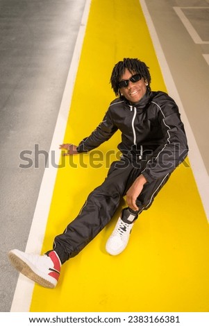 Vertical photo of an african modern musician sitting on the ground in an urban space