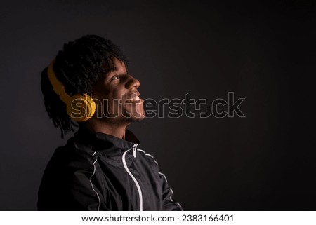Dark studio portrait of a young african man listening to music with headphones
