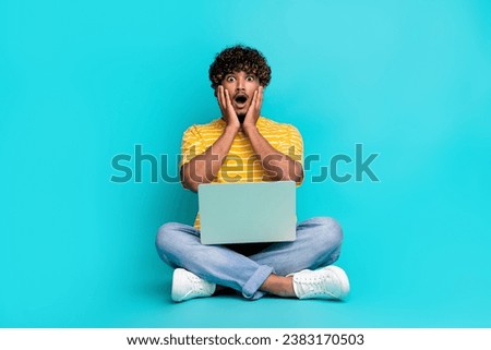 Full size portrait of impressed speechless guy sitting floor hold netbook hands touch cheeks isolated on turquoise color background