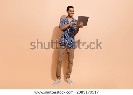 Full size photo of intelligent man wear print shirt brown pants look at laptop in hand write email isolated on beige color background