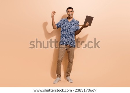 Full length photo of ecstatic man dressed blue shirt brown trousers scream yeah win bet hold laptop isolated on beige color background