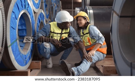 A male factory worker assists a female industrial worker who has an injured leg. As a result of working with hefty and huge objects Royalty-Free Stock Photo #2383187095
