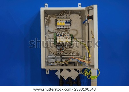 Power cabinet on wall. Electrical panel with open cover. Power cabinet with wires and circuit breakers. Blue wall with electricity control panel. Open power cabinet close-up. Electro technology Royalty-Free Stock Photo #2383190543