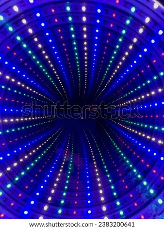 LED lights in blue, red, green and white dance in an elegant swirl against a deep, black background. The outline of a smartphone filming can be seen in the background.