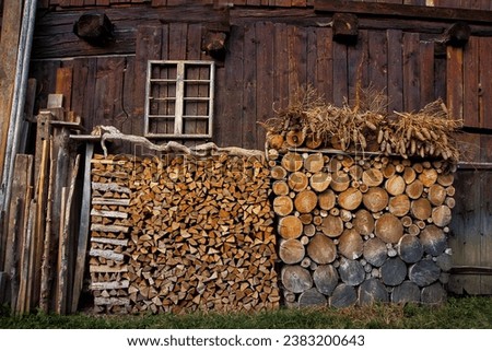 The picture shows an idyllic wooden hut with a varied pile of wood, surrounded by pine cones and a old window.