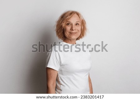 Close up of a 60s middle age woman smiling and wearing a white t-shirt on a white studio wall background Royalty-Free Stock Photo #2383201417