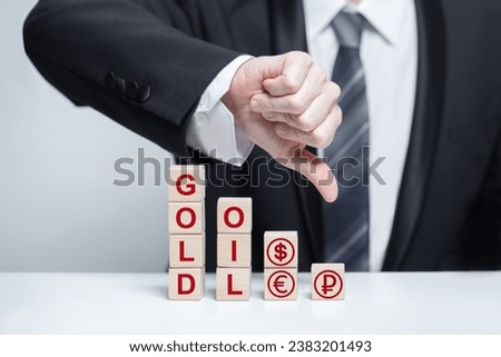 Word gold and currency icons on wooden blocks: euro, us dollar, ruble, bitcoin, pound sterling, yuan. Businessman thumb down. Gold, valuable metall, business concept