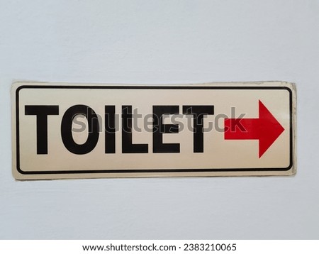 Sign of a worn sticker direction to the toilet on a white wall
