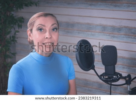 A girl in a blue turtleneck is preparing for a podcast with a microphone. Large ficus in the background