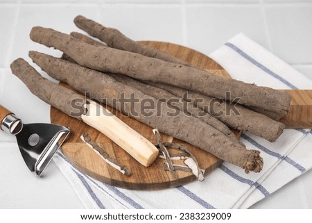 Raw salsify roots and peeler on white tiled table