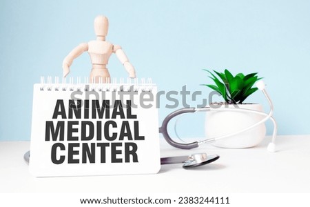 The text ANIMAL MEDICAL CENTER is written on notepad and wood man toy near a stethoscope on a blue background. Medical concept