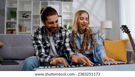 Funny portrait of smiling father with daughter playing synthesizer singing dancing and sitting sofa at light living room. Activity family love and lifestyle Concept Royalty-Free Stock Photo #2383251173