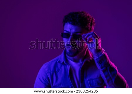 Studio shot of handsome smiling caucasian young man in stylish sunglasses isolated on gradient orange pink background in neon light. Copyspace for ad
