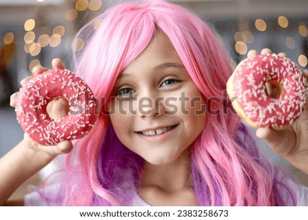 Close up Portrait of a little smiling girl with pink hair and two appetizing donuts in her hands, on a kitchen background. Vanilla Girl. Kawaii vibes.