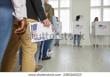 Diverse citizens at ballot station on election day. White and African American male and female voters holding voting forms in hands standing in line at polling place. Crop shot. US democracy concept  Royalty-Free Stock Photo #2383260225