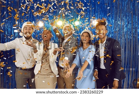 Cheerful overjoyed friends having fun at festive Christmas or New Year party. Group of happy joyful excited young diverse multiracial people in festive caps catching shiny golden confetti falling down
