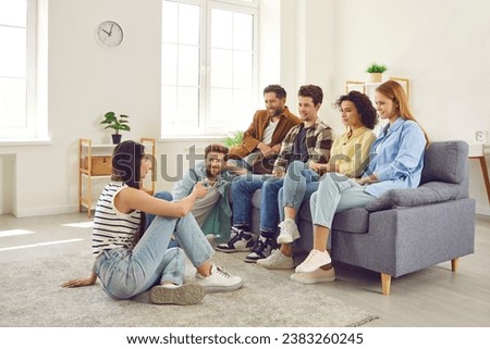 Group of friends hanging out together. Several young people meeting at somebody's place. Young men and women sitting on sofa and listening to girl who is sitting on floor and talking about something Royalty-Free Stock Photo #2383260245