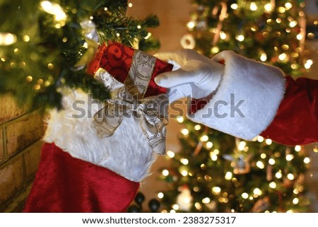 Santa Claus hand putting a present in a Christmas stocking hung on the fireplace on Christmas Eve