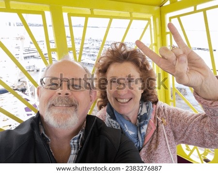 An excited couple take a selfie while riding on a ferris wheel to share on social media or with their family on a photo messaging group. Geelong promenade ferris wheel for tourists.