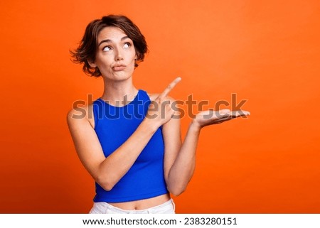 Photo of doubtful unsure lady wear blue singlet looking showing finger arm empty space isolated orange color background