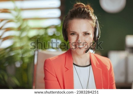 Sustainable workplace. Portrait of smiling modern business woman at work in a red jacket with headset. Royalty-Free Stock Photo #2383284251
