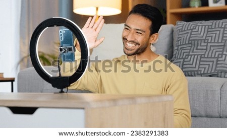 Influencer, ring light and smartphone, man wave at camera with social media, live streaming and video while at home. Content creation, communication with followers and tech, happy and subscription Royalty-Free Stock Photo #2383291383