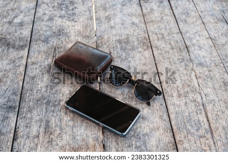 Traveling Essential Consists of Smart Phone, Wallet, and Sunglasses on Old Wooden Surface Background