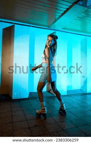 Young woman wearing comfortable sport clothes and roller skates posing in underground passage. Backlited background. Healthy lifestyle