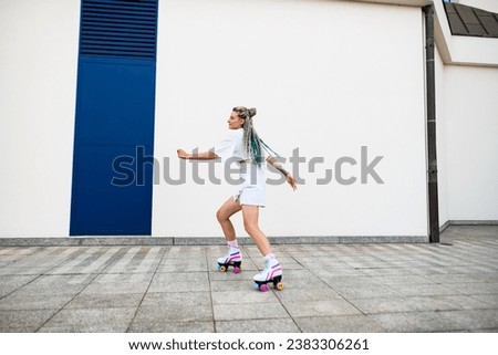 Young woman with colorful braids in hair skates on retro rollers outside against white wall background. Healthy way of life. Sport activity.