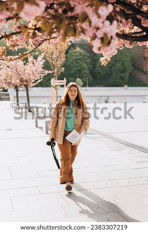 Attractive young female tourist is exploring new city. Redhead 30s girl holding a paper map and camera in Krakow. Traveling Europe in spring, full body