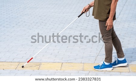 Close-up of the legs of an elderly blind woman with a cane at a tactile tile.