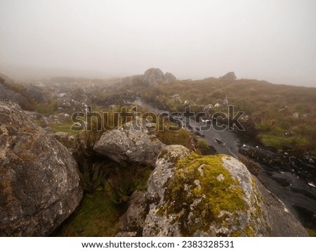 Irish nature scene with small creek in green fields with rocks and fog in the background. Connemara, Ireland. Hard weather conditions. Nature, travel and sightseeing.
