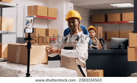African american girl in overalls filming PR video for social media, creating advertisement for warehouse storage in boxes. Woman recording video on smartphone, stock merchandise. Handheld shot.
