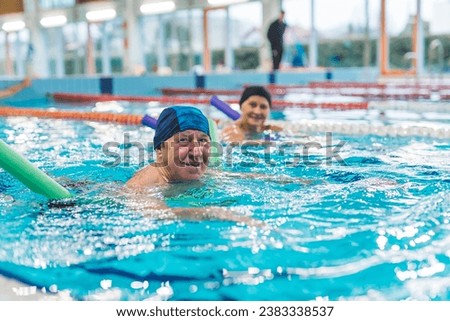 lovely European couple having swimming lesson with swim noodles in the indoor pool. High quality photo Royalty-Free Stock Photo #2383338537